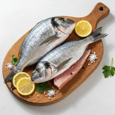 Fresh dorado fillets on a wooden cutting board with lemon and herbs
